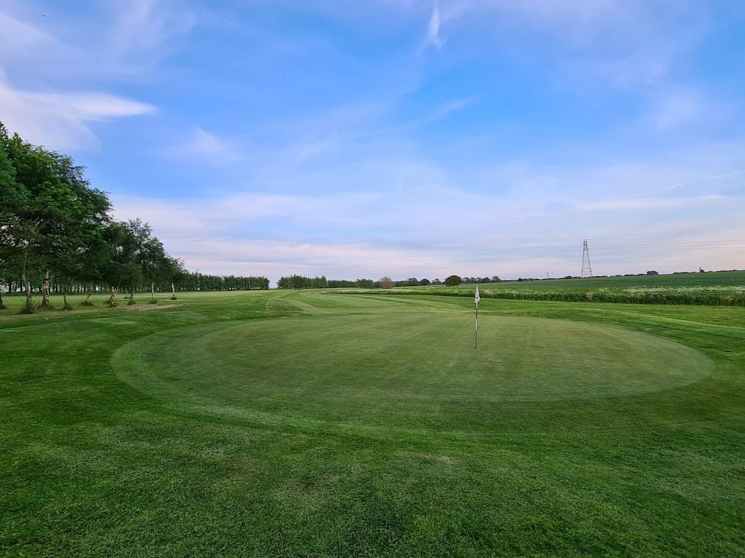 Lush green golf course with a flag on the putting green under a blue sky in Thorpe Willoughby, Yorkshire.