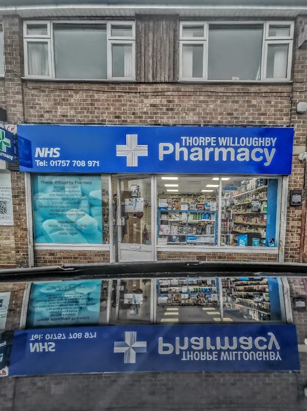 Thorpe Willoughby Pharmacy storefront with blue signage, NHS logo, and window displays of health products.