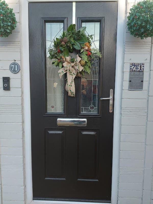 A decorated front door with a wreath featuring greenery and a bow, flanked by two hanging plants.