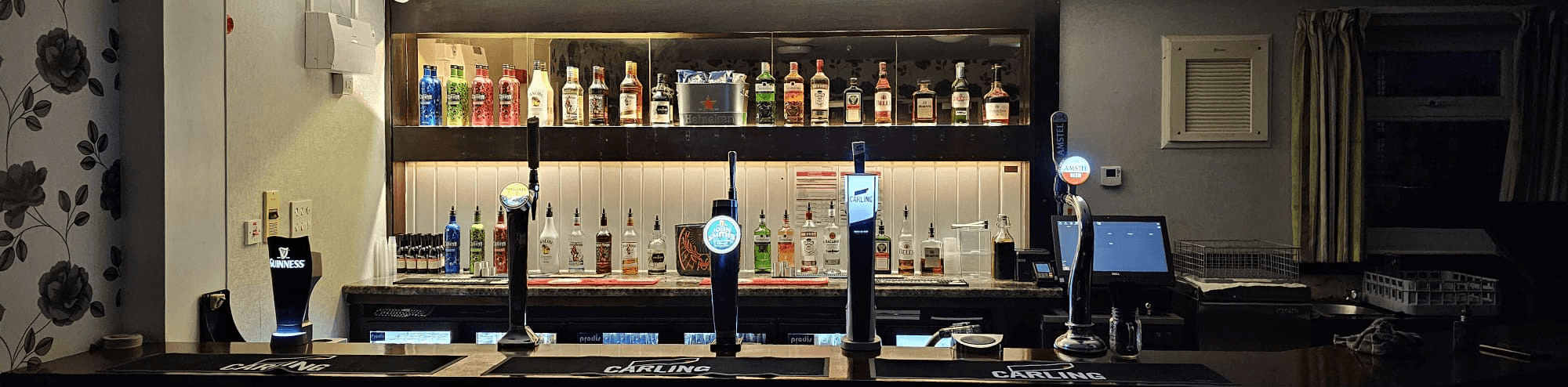 Bar area with illuminated beer taps, shelves of liquor bottles, and a stylish counter in a cozy venue setting.