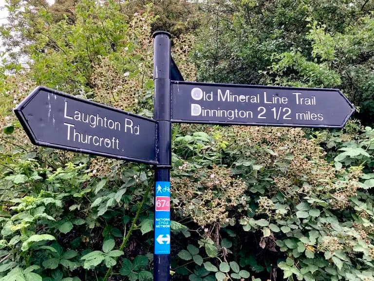 Signpost directing to Laughton Rd, Thurcroft, and the Old Mineral Line Trail, with greenery in the background.
