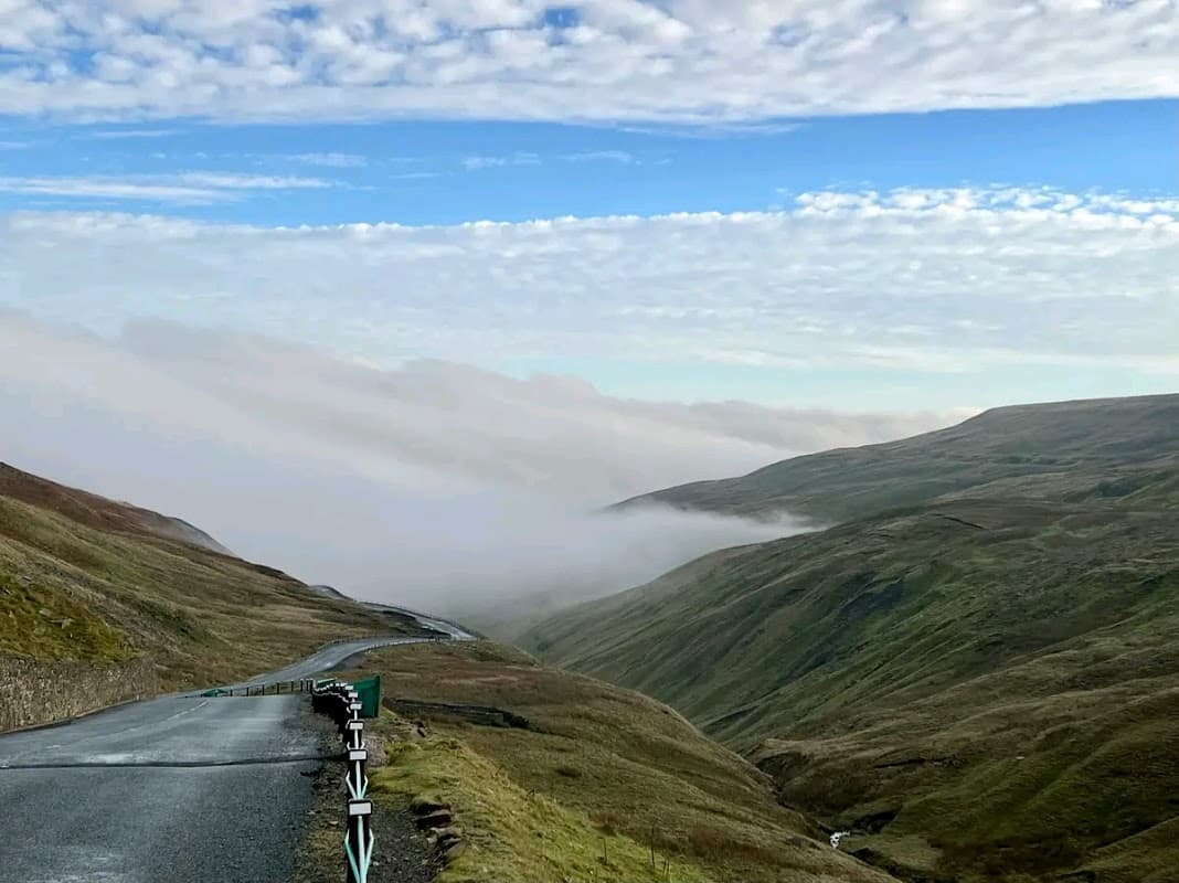 Scenic view of Buttertubs Pass with winding road, rolling green hills, and misty valleys under a cloudy sky.