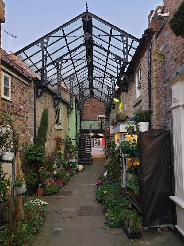 Free car park in Tickhill, Yorkshire, featuring a glass-roofed walkway and vibrant flower displays along the path.