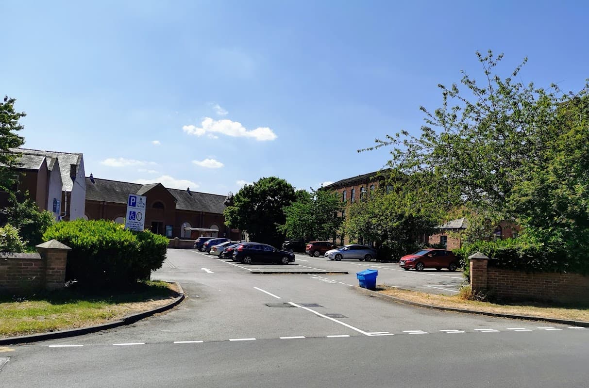 Free parking area with several cars, trees, and a blue bin under a clear blue sky in Tingley, Yorkshire.