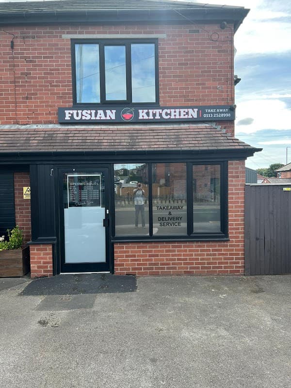 Fusian Kitchen restaurant with a red brick exterior, large windows, and a sign indicating takeaway and delivery services.