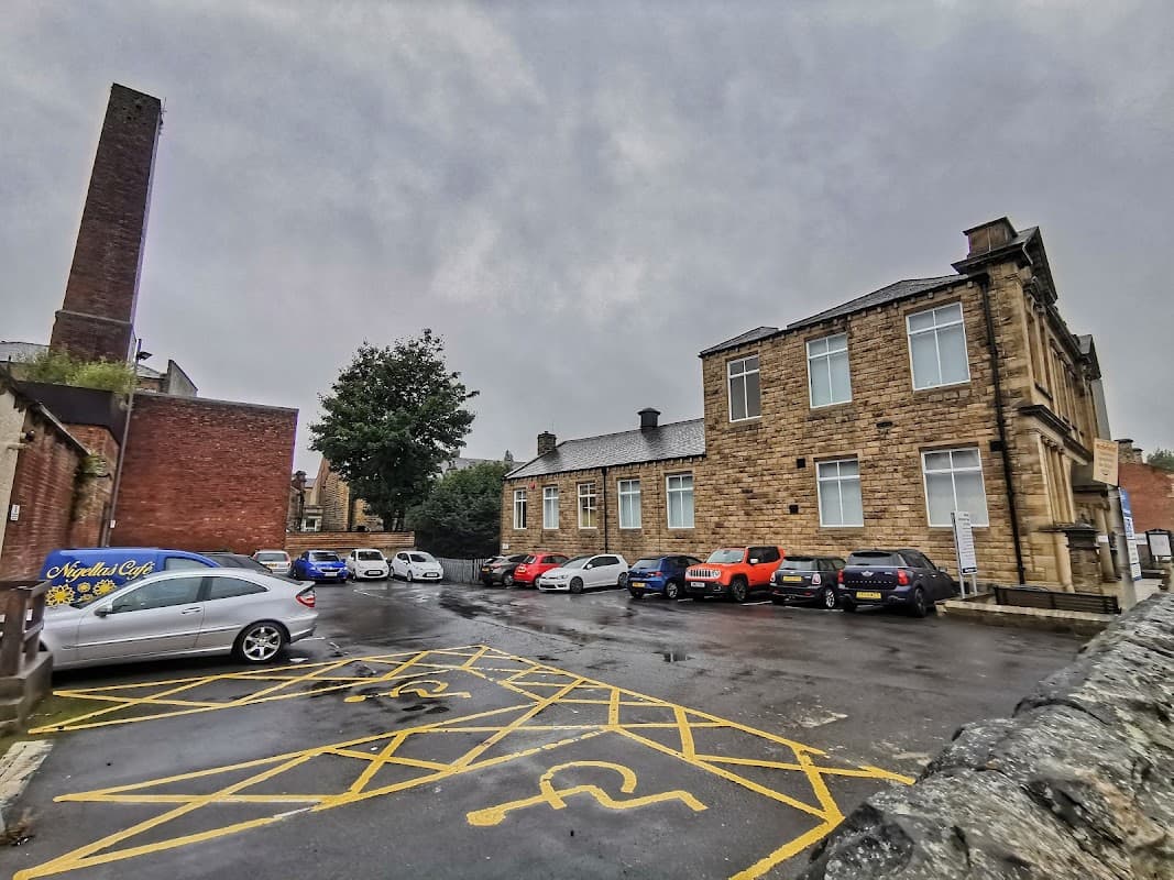 Morley Library Car Park with several parked cars, a stone building, and a cloudy sky in Tingley, Yorkshire.