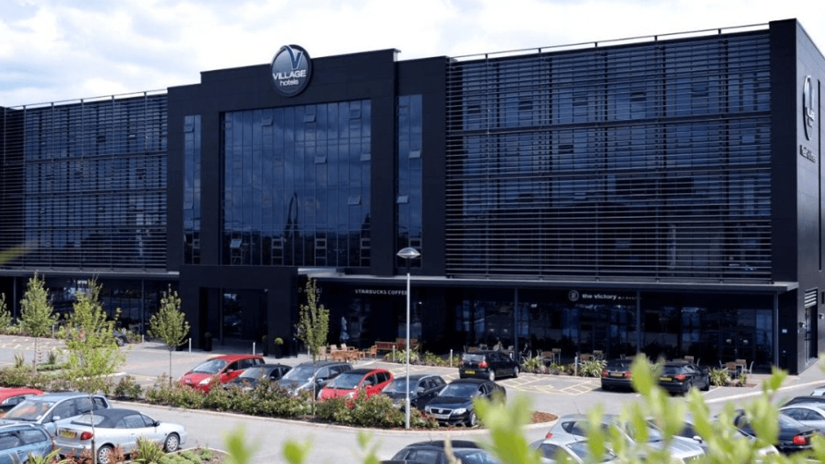 Modern black hotel building with large windows, surrounded by parked cars and landscaped greenery in Tingley, Yorkshire.