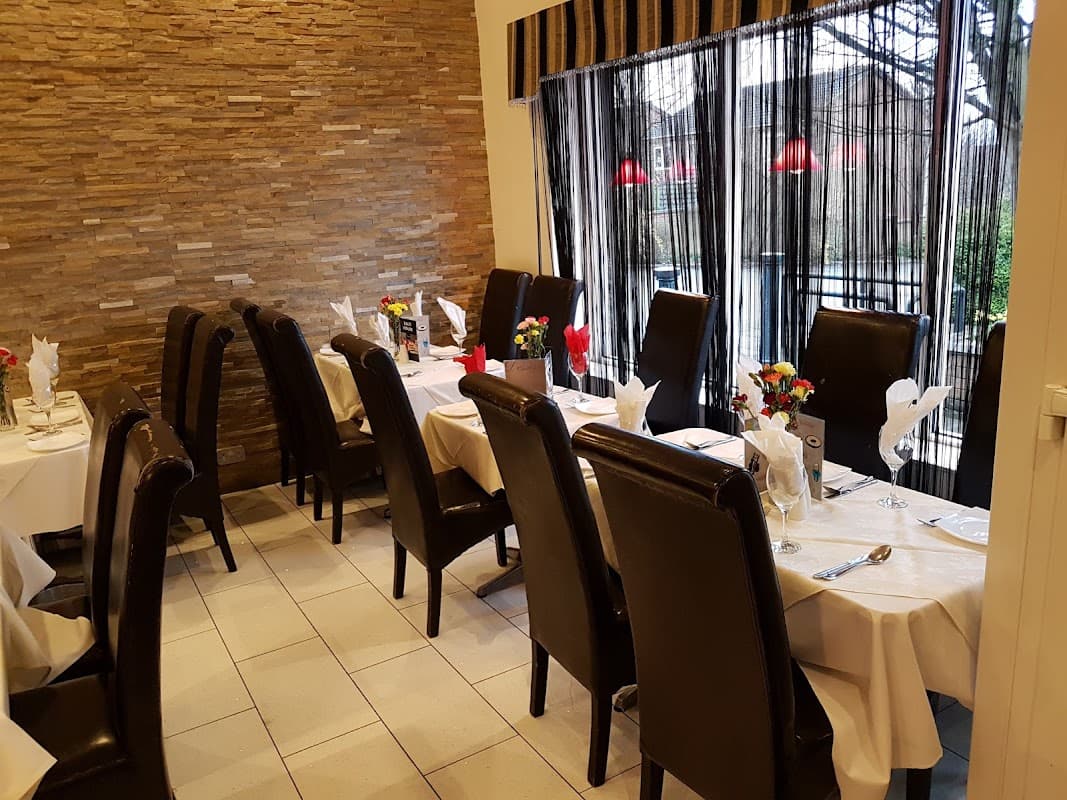 Cozy dining area with brown leather chairs, white tablecloths, flowers, and large windows draped with sheer curtains.
