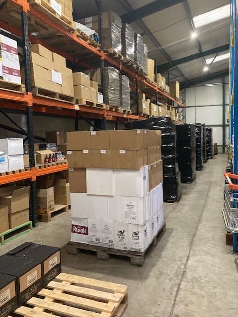 A warehouse interior with stacked pallets of boxed beer and shelves filled with various beverages in Tockwith, Yorkshire.