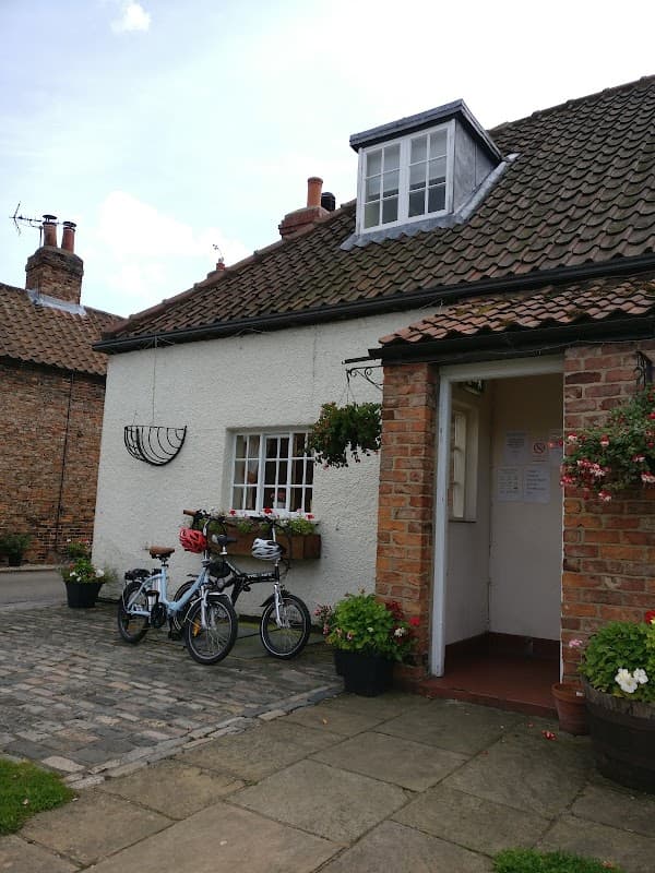 Charming hotel exterior with a thatched roof, flower baskets, and two bicycles parked on a cobblestone path.