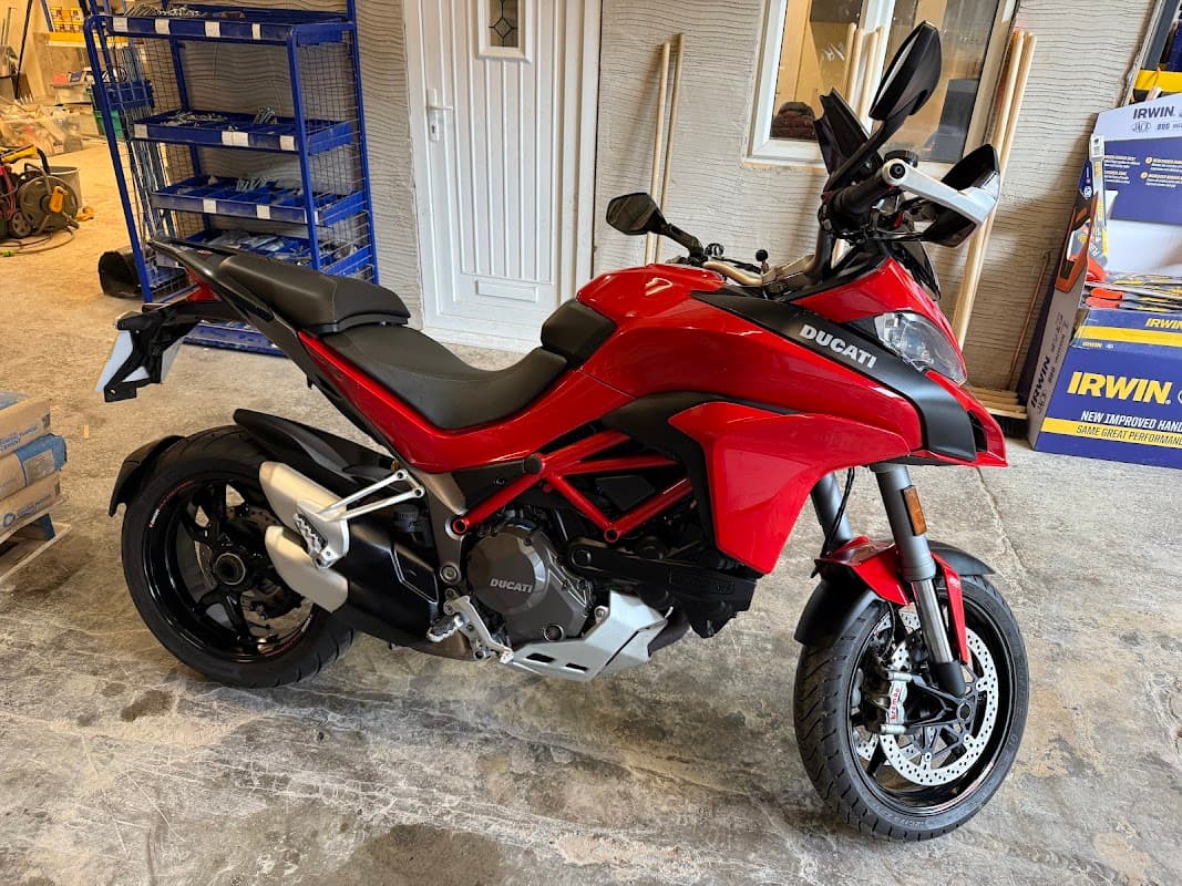 Red Ducati motorcycle parked in a workshop with tools and equipment in the background.