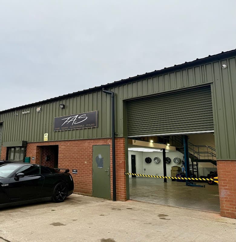 TAS Auto Centre LTD shopfront with a green exterior, garage door, and a black car parked outside.