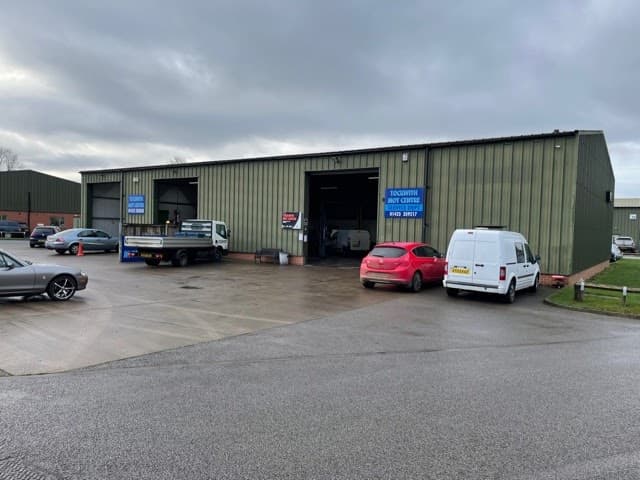 Exterior of Tockwith Mot Centre Ltd, featuring a large green industrial building, vehicles parked outside, and signage.