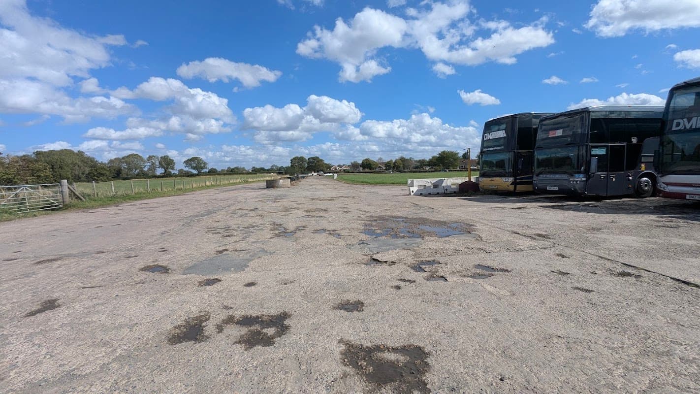 Tockwith Multi Drive Centre with parked buses, a gravel lot, and a blue sky with scattered clouds.