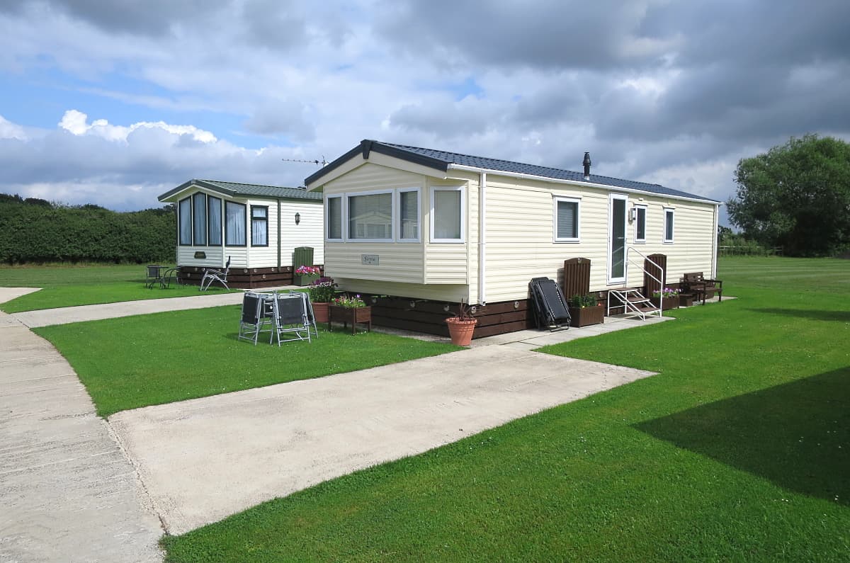Two static caravans on a grassy campsite, with a concrete path and cloudy sky in the background.