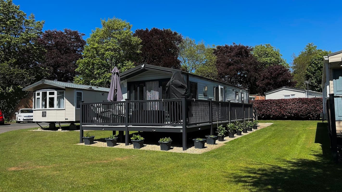 Modern holiday home with a deck, surrounded by potted plants and green grass, under a clear blue sky.