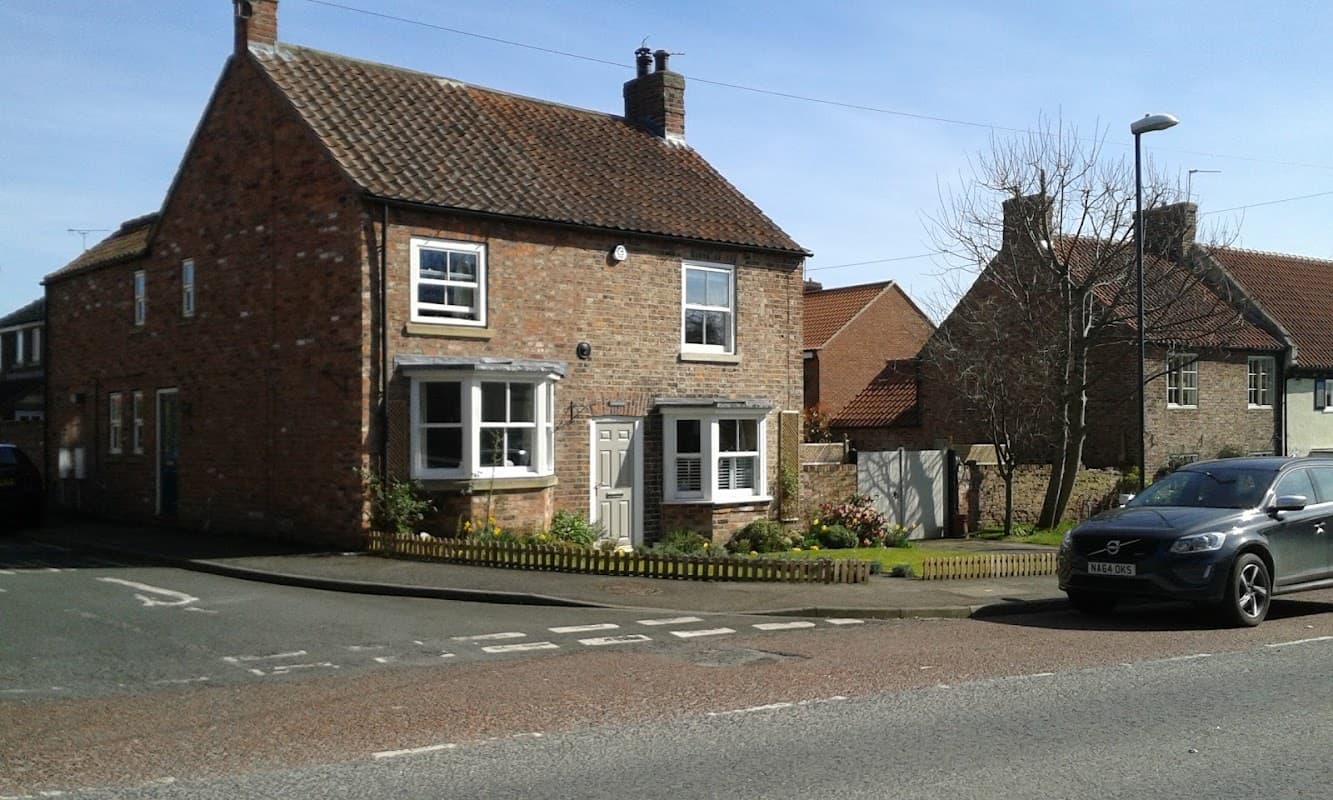 Topcliffe Village Hall, a brick building with a pitched roof, surrounded by greenery and residential homes.