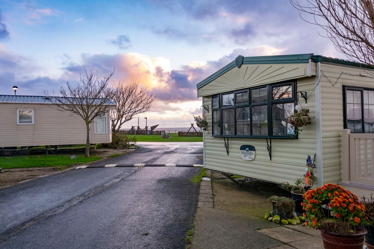 A holiday park with caravans, a paved road, and colorful flowers under a cloudy sky in Tunstall, Yorkshire.