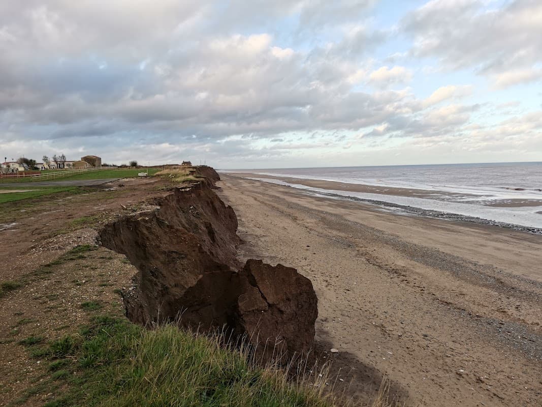 Eroded cliff edge overlooking a sandy beach with gentle waves and cloudy sky in Tunstall, Yorkshire.