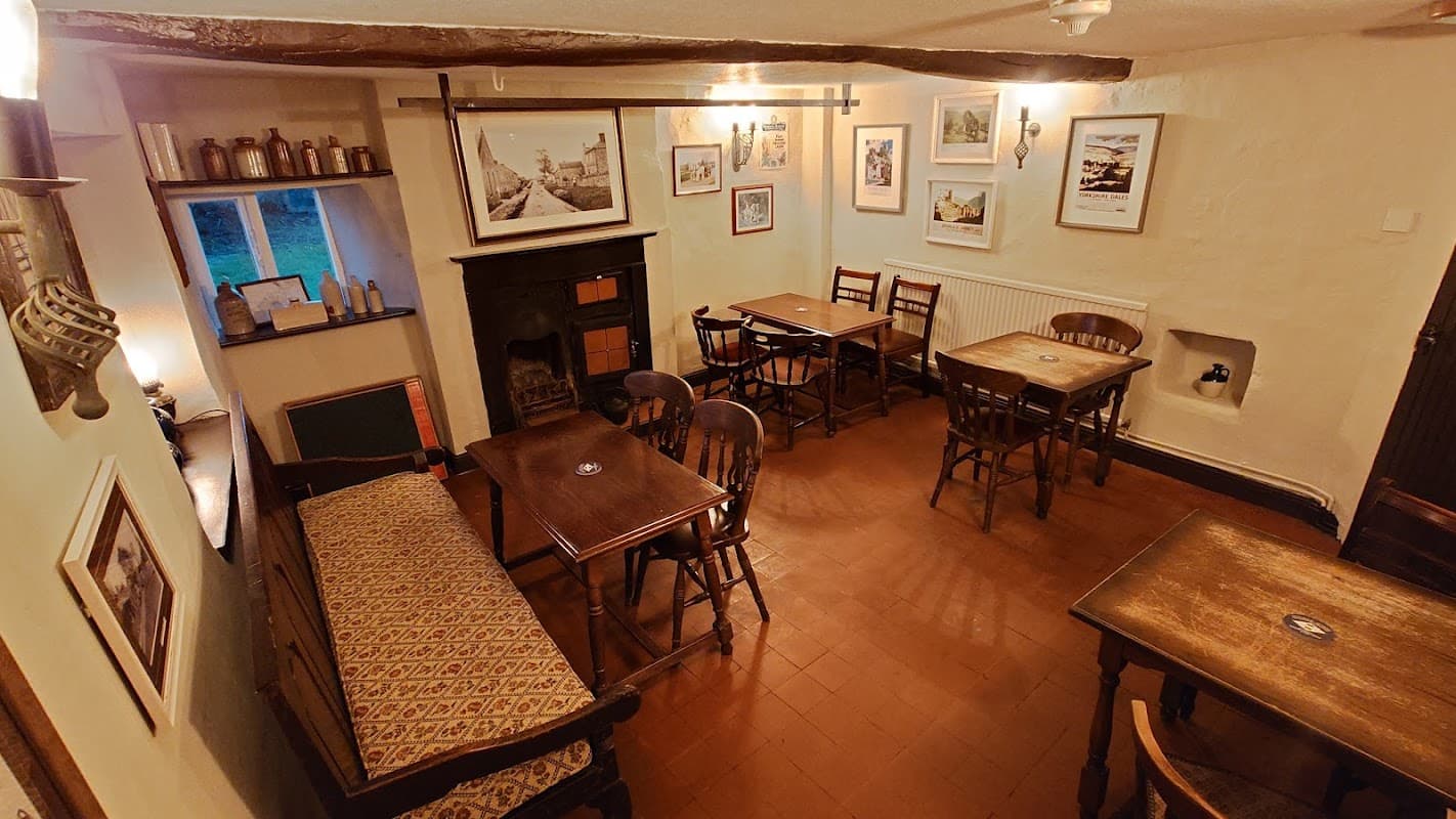 Cozy bar interior with wooden tables, chairs, a fireplace, and framed artwork on the walls.