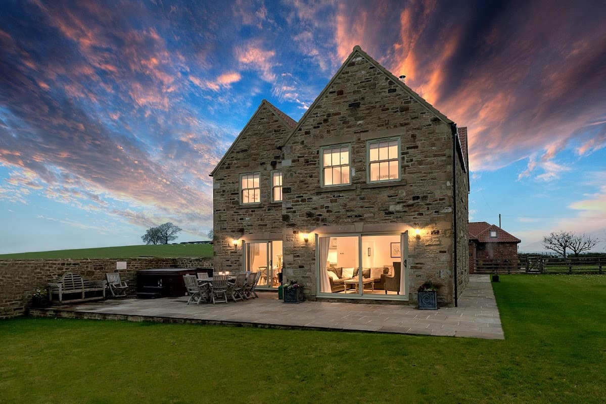 Stone farmhouse with large windows, patio area, and scenic sky at dusk in Tunstall, North Yorkshire.