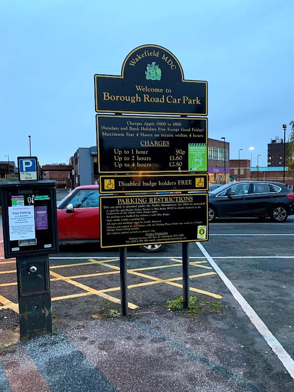 Welcome sign for Borough Road Car Park with parking charges and restrictions, surrounded by parked cars and buildings.