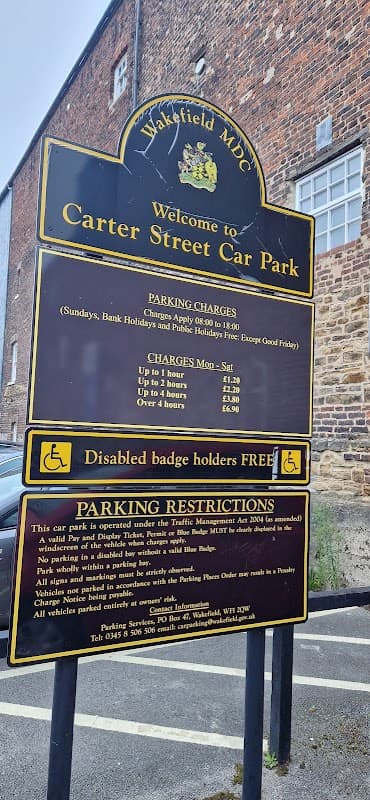 Welcome sign for Carter Street Car Park, detailing parking charges and restrictions, with a brick building in the background.
