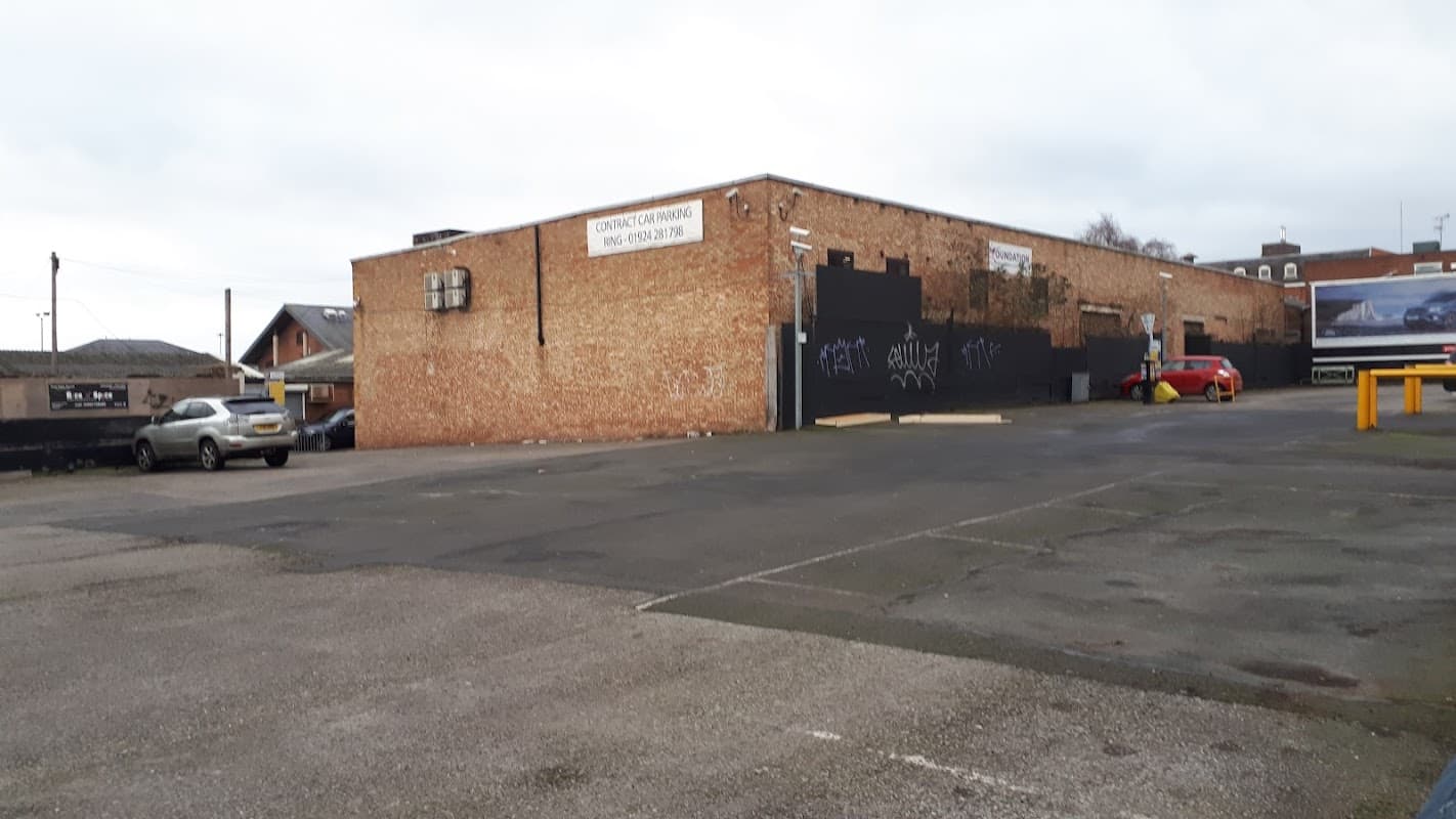 Brick wall of George Street Car Park with parked cars and graffiti, set in an urban environment in Wakefield, Yorkshire.