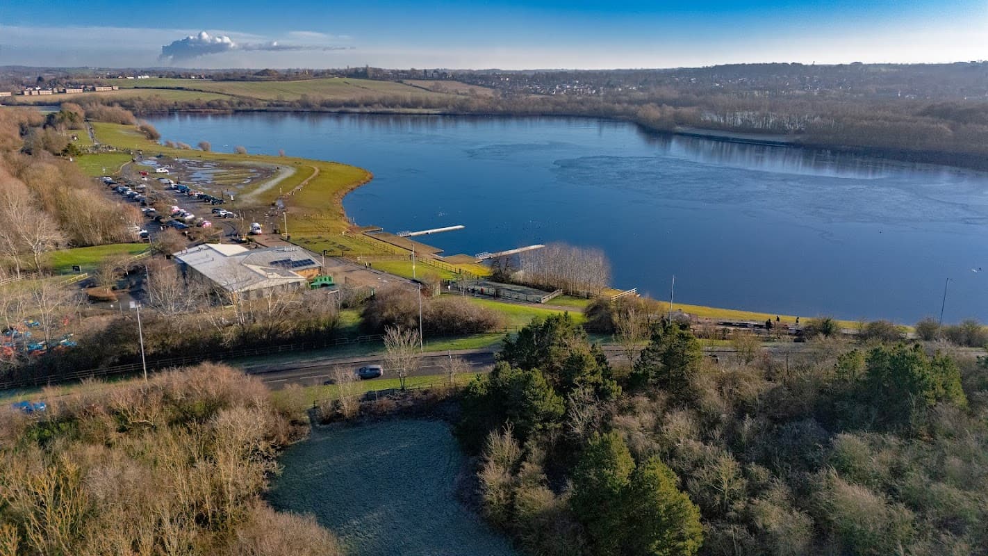 Pugneys Country Park car park beside a lake, surrounded by greenery and distant hills under a clear blue sky.