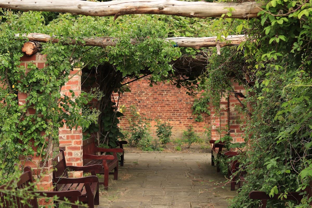 Overgrown archway with wooden benches, brick walls, and greenery in Thornes Park Stadium Car Park, Wakefield.