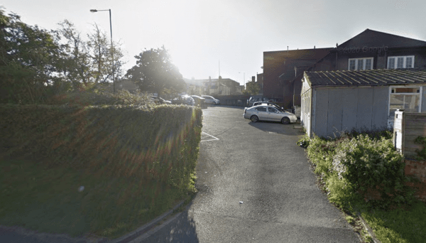 Car park with several vehicles, surrounded by greenery and buildings under bright sunlight in Wakefield, Yorkshire.