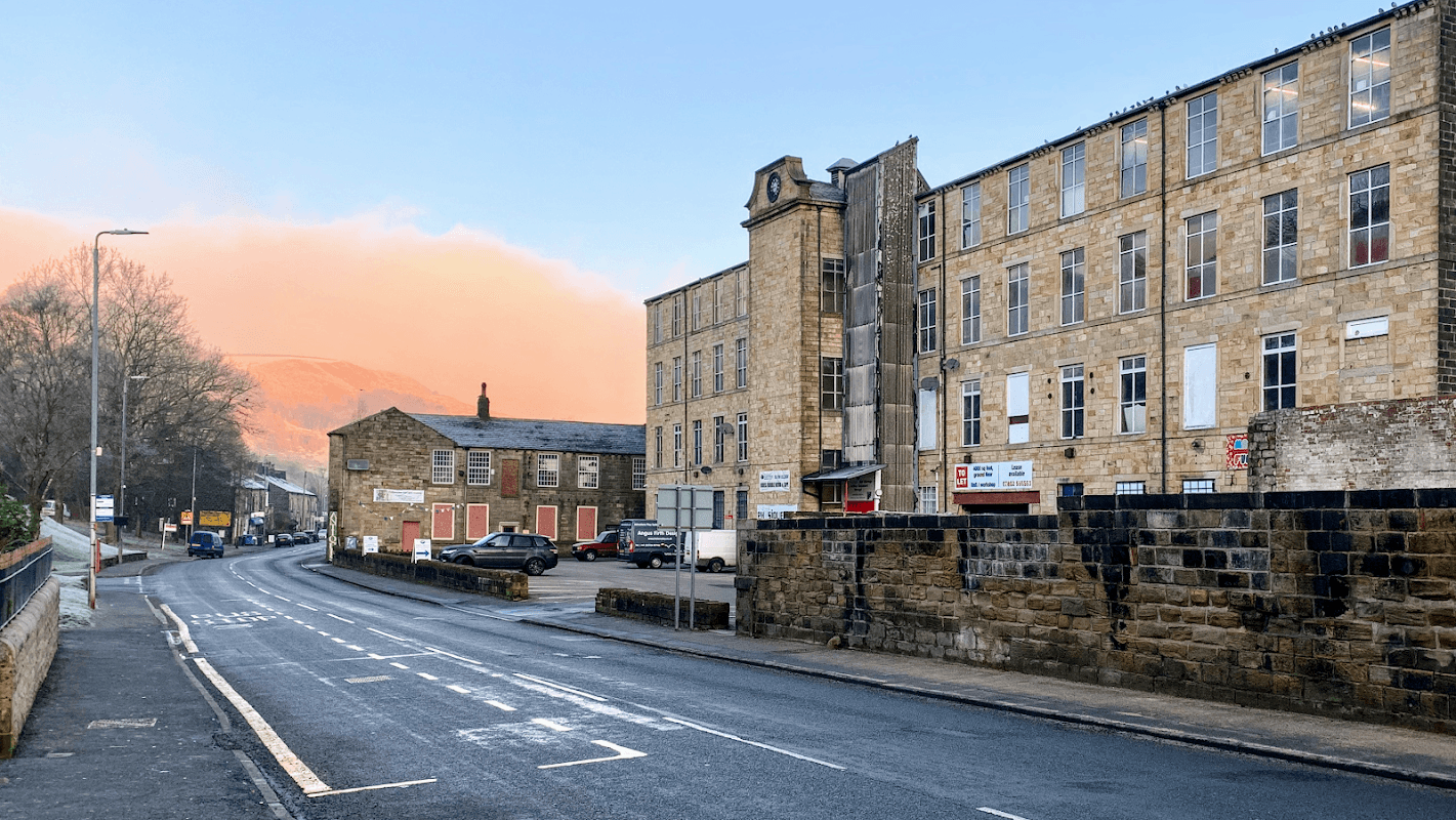 Roch Valley Self Storage building on a quiet street, with stone architecture and a backdrop of hills under a colorful sky.