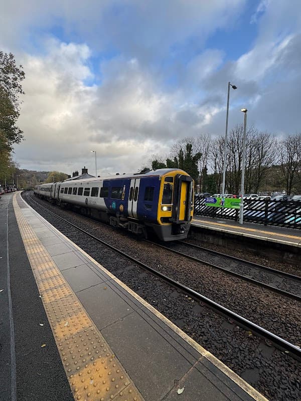 Train approaching the Todmorden station, with tracks and trees lining the background under a cloudy sky.