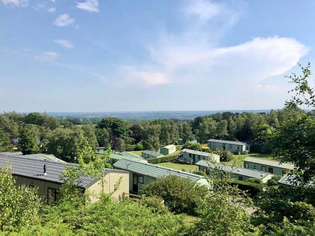Scenic view of Warren Forest Park with green lodges nestled among trees and rolling hills under a blue sky.