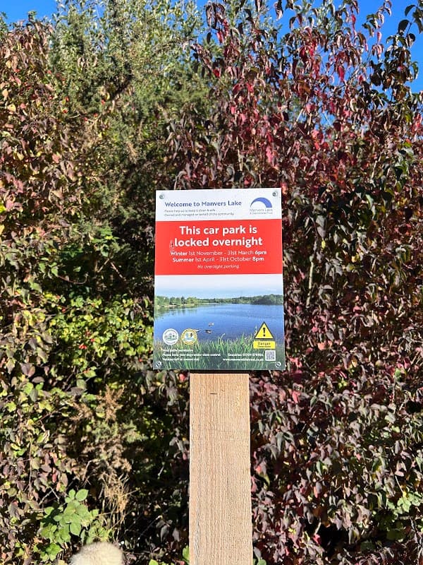 Sign indicating car park hours, surrounded by greenery and trees, with a scenic lake in the background.