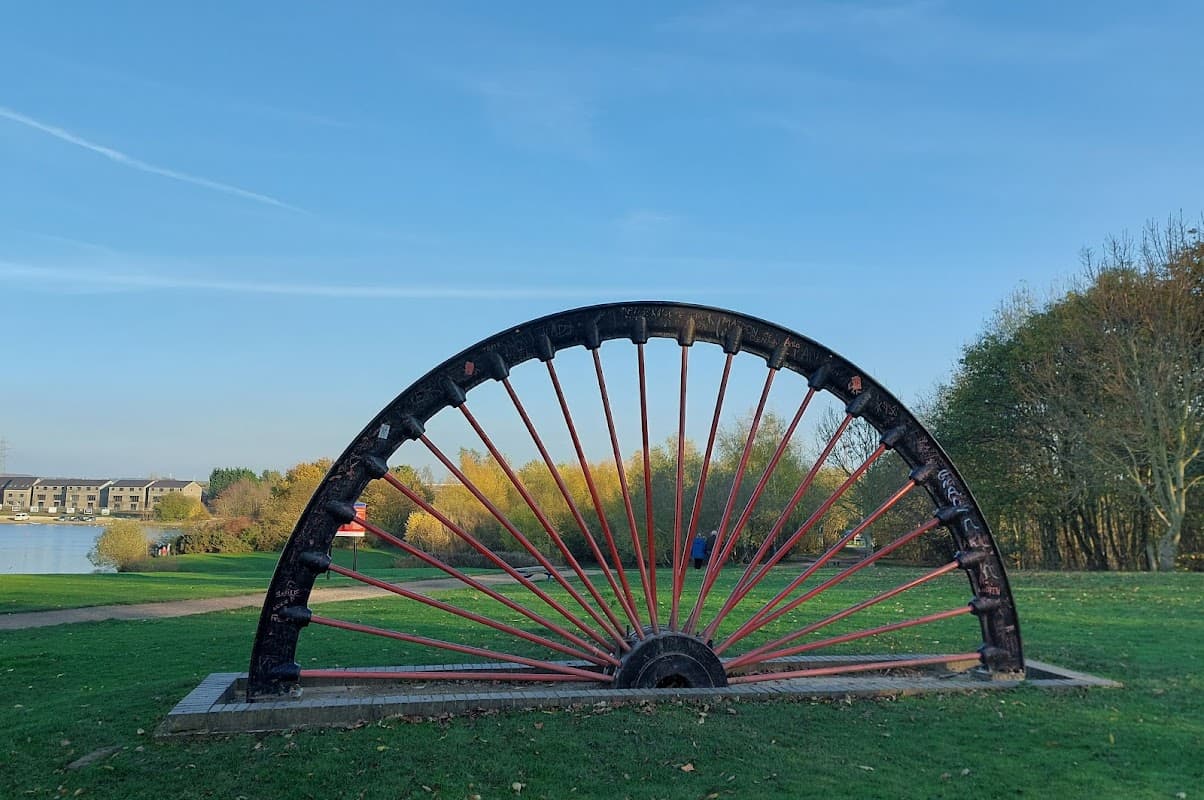 Wath Main Pit Head Winding Wheel stands prominently against a clear blue sky, surrounded by greenery and a lake.