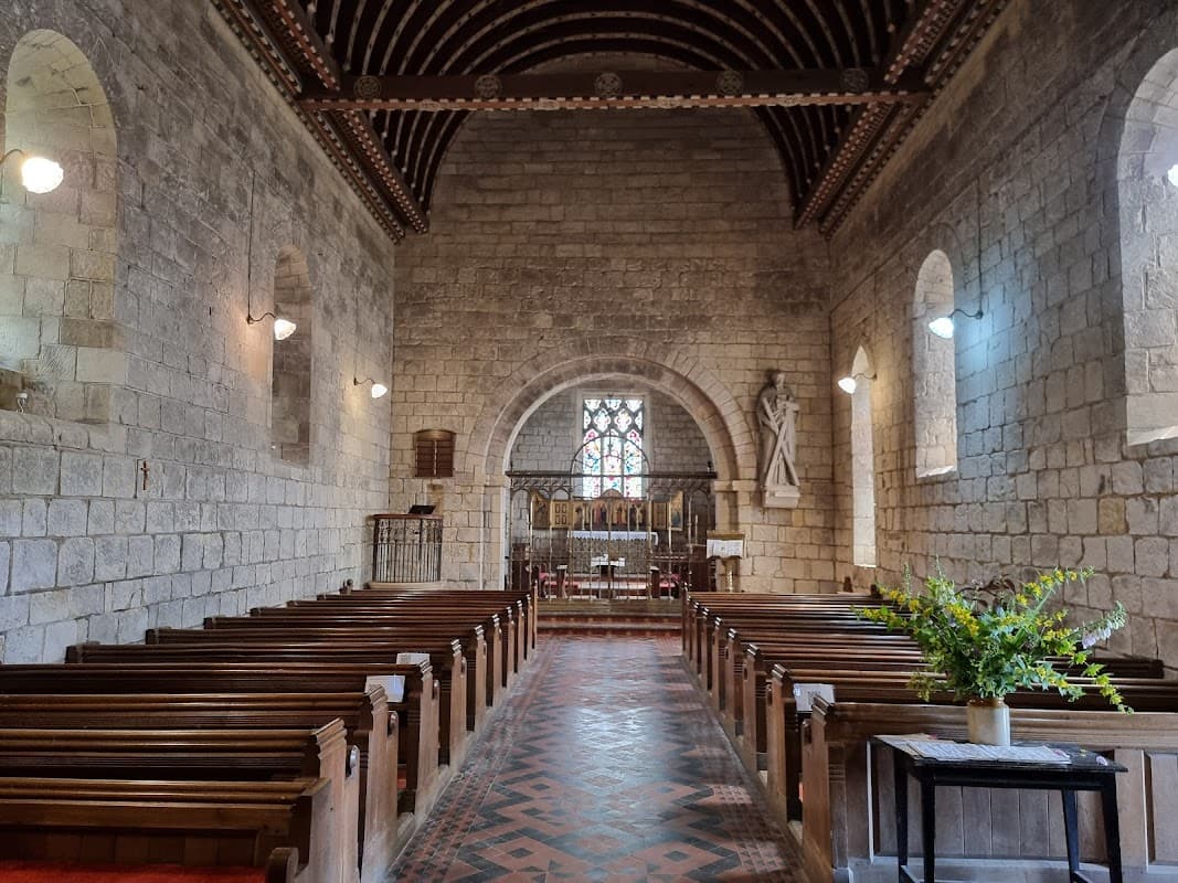 Interior of St Andrew's Church featuring wooden pews, stone walls, stained glass windows, and a decorative ceiling.