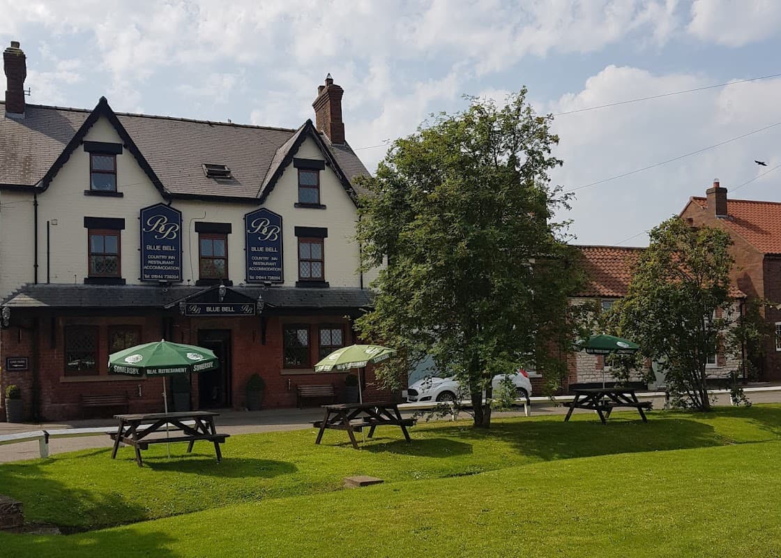 The Blue Bell Inn in Weaverthorpe, featuring outdoor seating and green umbrellas on a sunny day.