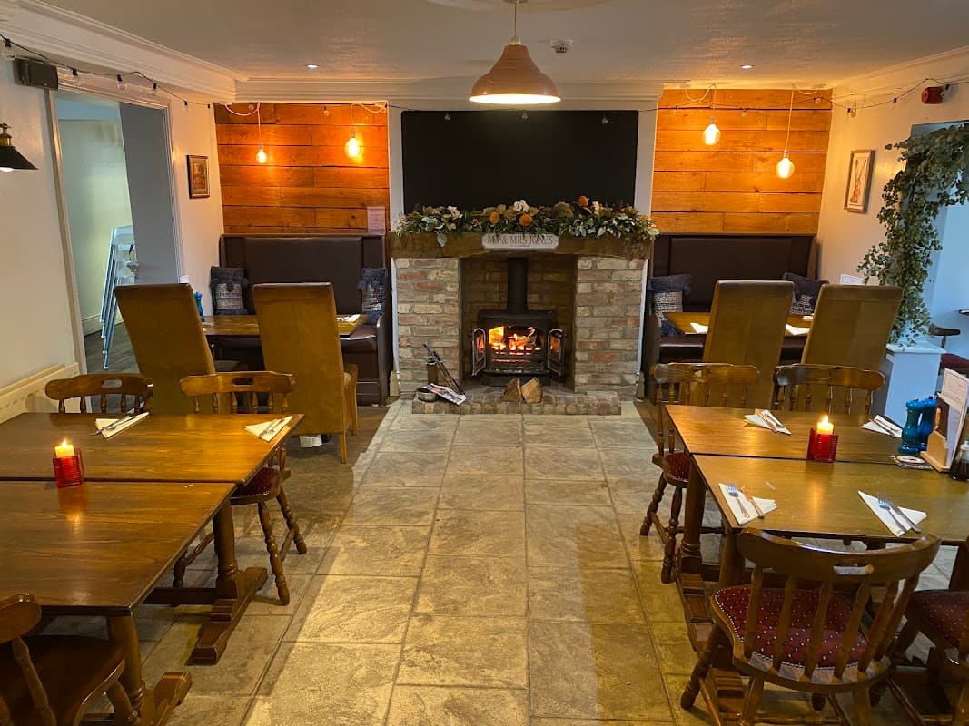 Cozy bar interior with wooden tables, chairs, a brick fireplace, and decorative plants in Welbury, Yorkshire.