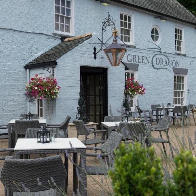 Light blue exterior of the Green Dragon bar, featuring hanging flower baskets, outdoor seating, and lanterns.