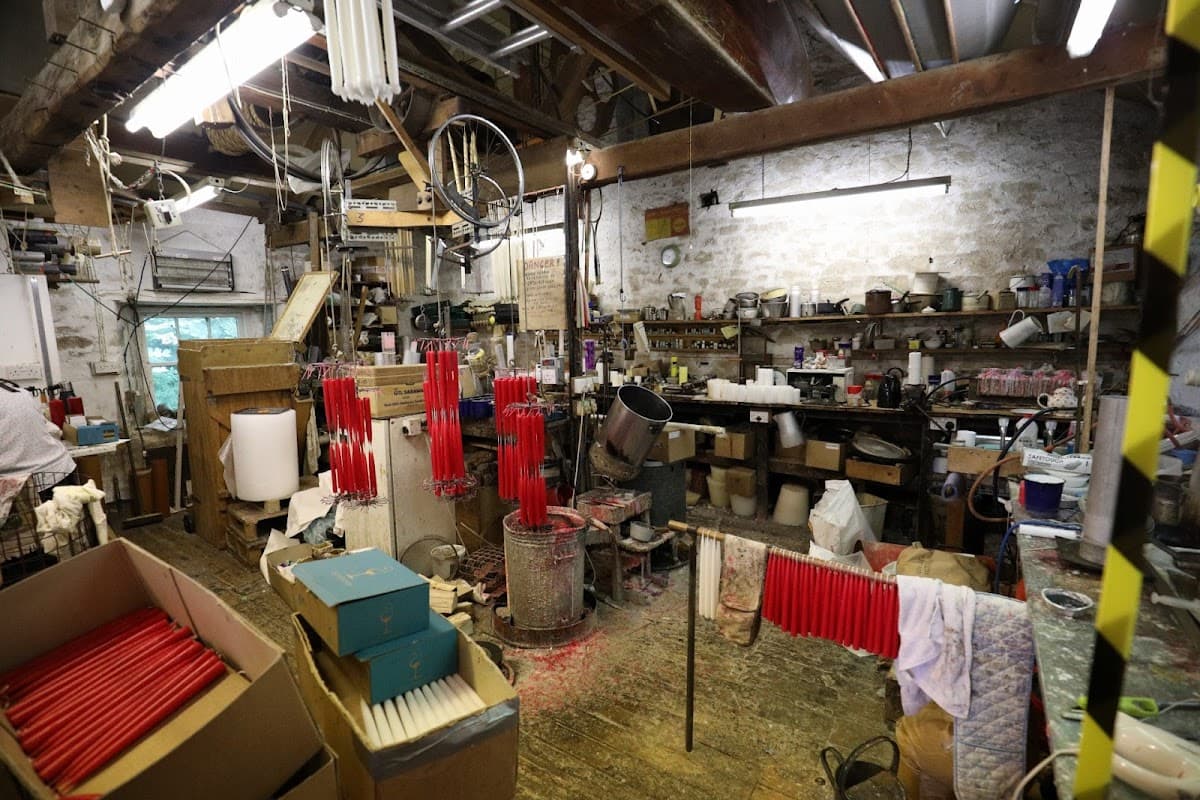Workshop interior with red candles hanging, shelves filled with tools, and boxes scattered around a rustic space.