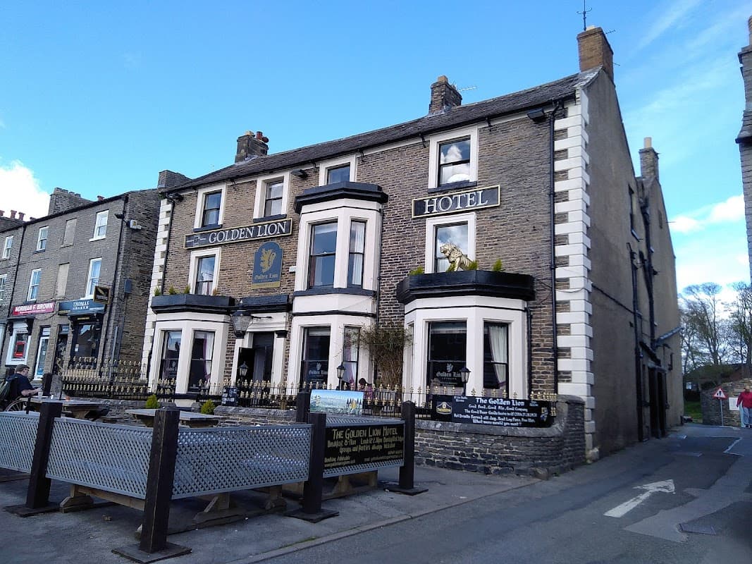 Historic stone building with "Golden Lion Hotel" signage, featuring a lion statue and outdoor seating area.