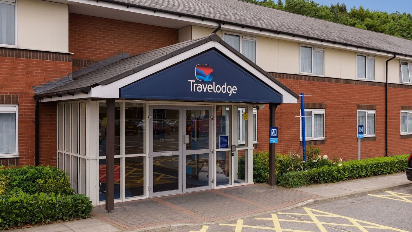 Travelodge entrance with a blue canopy, brick facade, and accessible parking in a green, landscaped area.