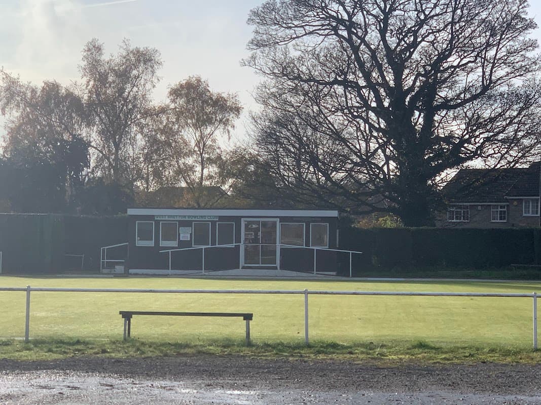 West Bretton Bowling Club building with large windows, surrounded by green lawn and trees, under a cloudy sky.