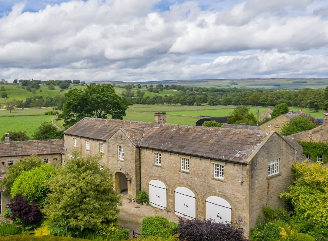 Cottages with stone facades surrounded by lush greenery and rolling hills under a cloudy sky in West Burton, Yorkshire.