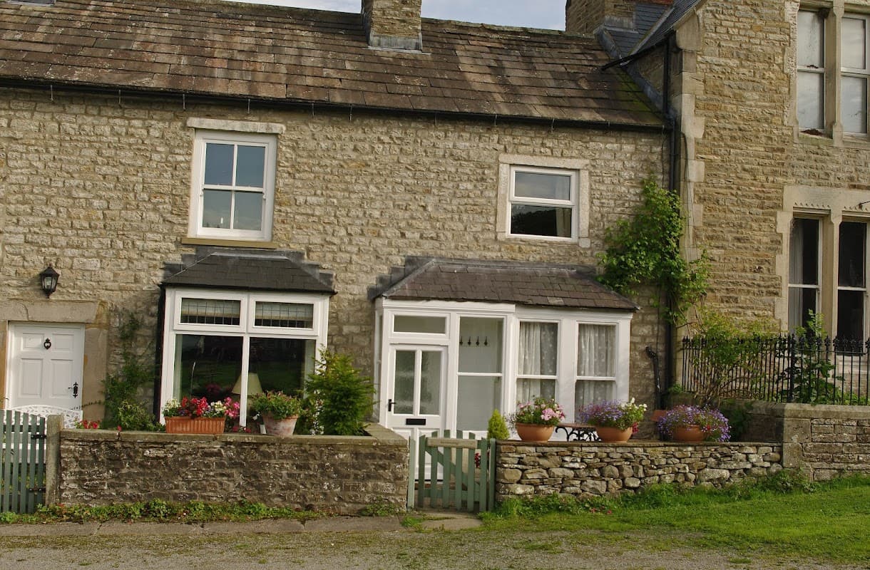 Stone cottage with flower-filled window boxes and a small garden, set in a rural Yorkshire landscape.