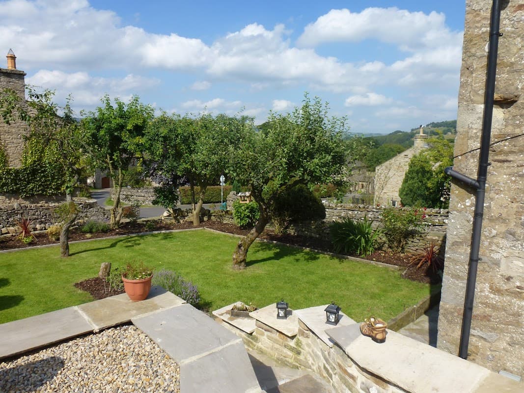 Quaint garden with trees, stone walls, and a clear blue sky in West Burton, Yorkshire, near Flag Cottage.