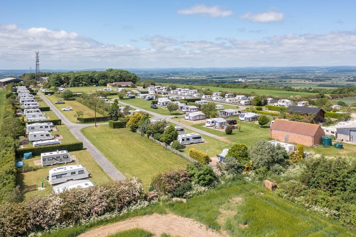 Expansive view of Wolds Way Caravan and Camping, featuring neatly arranged caravans and lush green fields under a blue sky.