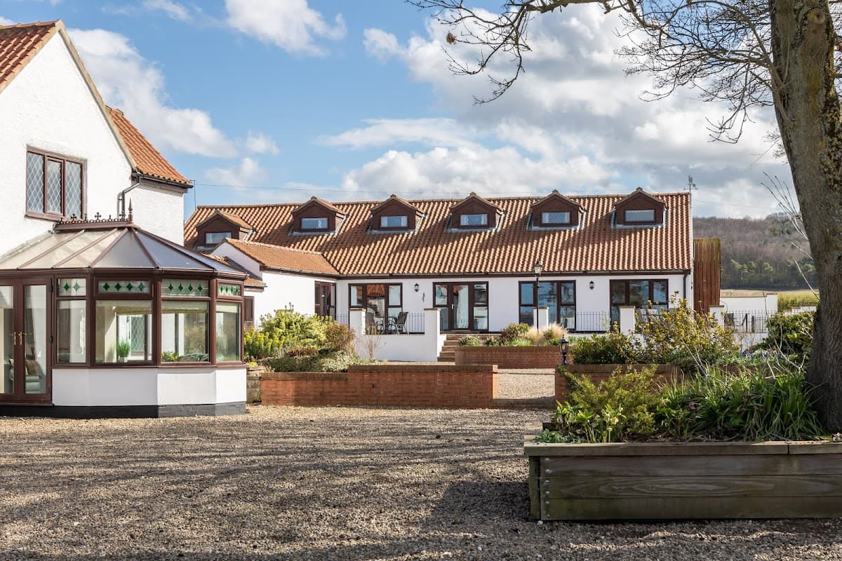 Charming hotel with a red-tiled roof, landscaped gardens, and a glass conservatory under a blue sky in West Knapton.