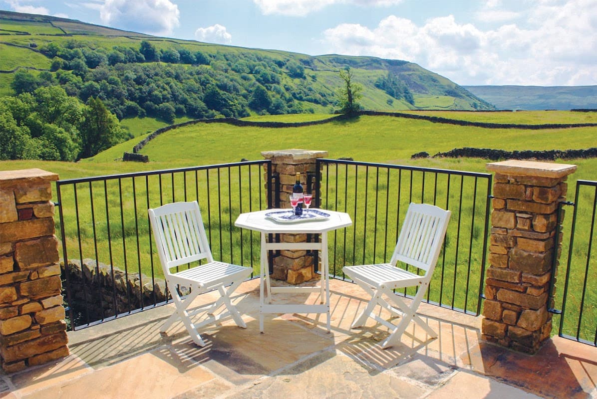 Cozy patio with white chairs and a table overlooking lush green hills and stone walls in West Stonesdale, Yorkshire.